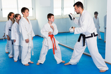 Teenagers are practicing on boxing paws with coach during karate class.