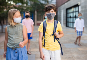 Confident preteen girl and boy in protective masks walking with other schoolchildren to school campus after lessons on warm spring day. Concept of necessary precautions in COVID pandemic