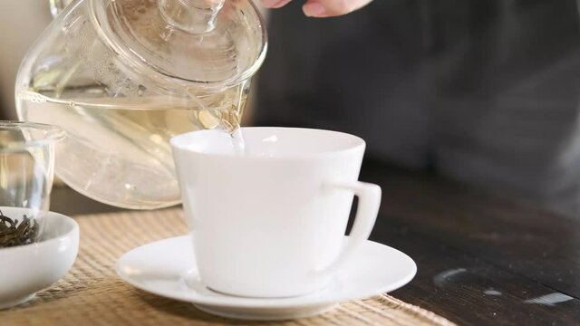 woman's hand pouring hot tea from the teapot into the teacup on wooden table 4k