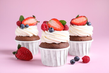 Delicious cupcakes with cream and berries on pink background