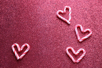 Christmas background. Four candy cane hearts on red glitter background.