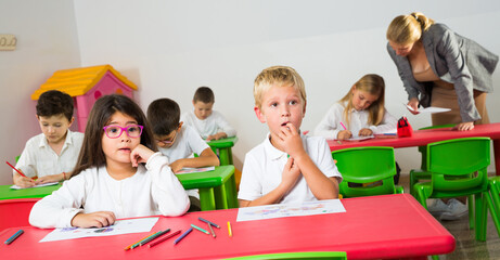 Portrait of surprised little pupils at lesson in classroom at elementary school..