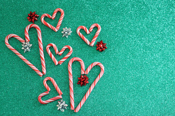 Christmas background. Large and small candy cane hearts surrounded by red and silver bows on green glitter background.