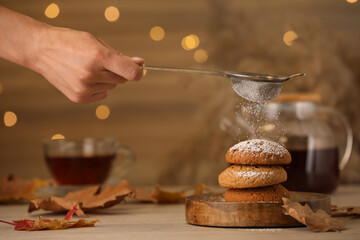 Woman sieving icing sugar on cookies at wooden table, closeup