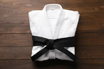 Martial arts uniform with black belt on wooden background, top view