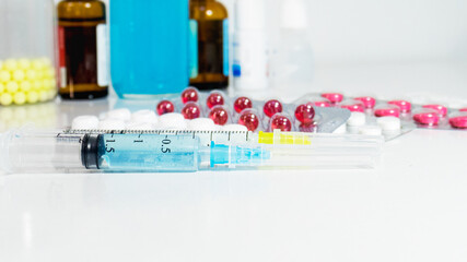 On the table are injecting syringes and various tablets, and in the background are medicinal syrups and also various drops and vitamins. Blurred background. Selective focus. syringes and injections. 
