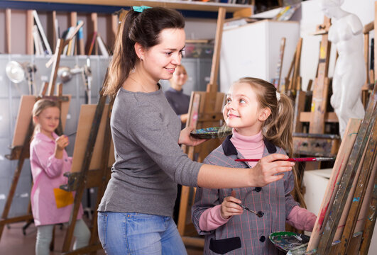 Smiling woman teacher assisting girl during drawing class at art studio