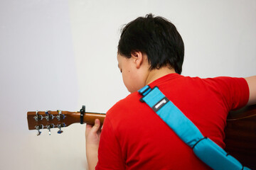 photo from behind black haired boy playing guitar with chords and capo and has a sash sitting in...