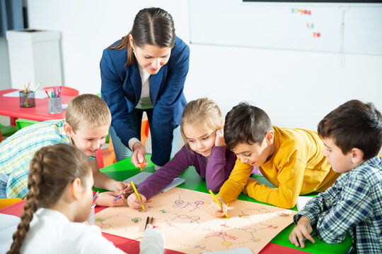 Pretty boys and girls with teacher draw a table game in classroom. High quality photo