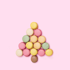 Fototapeta na wymiar Different colors fresh yummy macarons arrangement. Christmas tree inspired minimal concept. Flat lay with baby pink background.