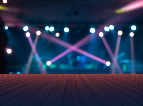 Empty table board with blurry bokeh. Stage concert with colorful lighting laser beam spotlight show in disco pub club bar background for party music dancing festival performance. Entertainment night