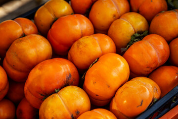 Ripe juicy persimmon in sunlight in a box on the market. Close-up. Vitamins and health from nature.