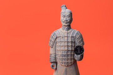A coin in denomination of one Chinese yuan and a souvenir figurine of a Chinese war famous from the terracotta army of Emperor Qin Shi Huang on a red background.