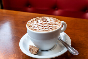 Close up white coffee cup with decorated shaped latte foam on wooden table in Brazil