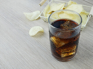 Soft drink and potato chips on wooden background.