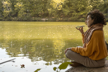 Brunette woman seated sending voice message on mobile phone