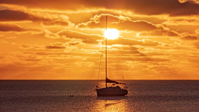 Anchored sailboat in Kuto Bay moves with currents during vibrant sunset timelapse
