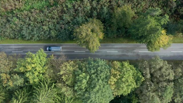 Fast driving blue lorry filmed from above, flying with a drone over the street in the autumnal season, concept for fast delivery service.