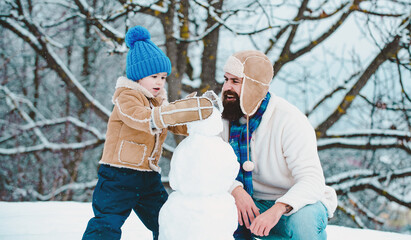 Winter, father and son play outdoo making snowman. Handmade funny snow man. Christmas family holidays with daddy. - Powered by Adobe