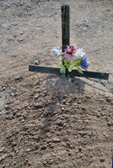 Small handmade wooden cross decorated with multi-colored silk flowers in a Mexican cemetery in Arizona. 