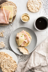Top view of Modern  healthy breakfast. Round buckwheat and rice cake with hummus, ham and cheese and coffee on white table .
