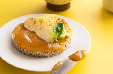 Close up buckwheat and rice snack with almond butter and apple decorated with cinnamon and basil on yellow background,