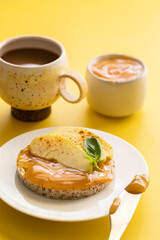 Crounchy buckwheat and rice snack with almond butter and apple decorated with cinnamon and basil on yellow background with cup of coffee