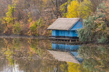 Fototapeta na wymiar An Old Wooden Building Surrounded by Colorful Trees is Beautifully Reflected on the Lake Surface on a Cloudy Autumn Day