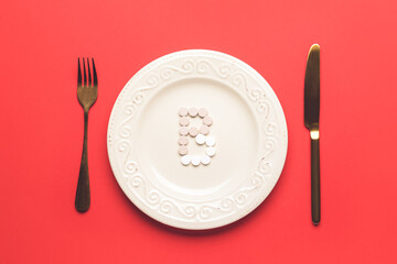 Letter B made of pills and plate with cutlery on color background