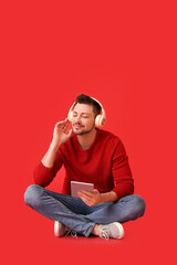 Man with tablet computer and headphones on color background