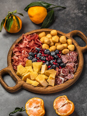 Assorted antipasti. Assorted cheese, berries and prosciutto. Tangerines with leaves. Christmas background.
