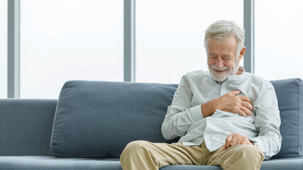 Fototapeta premium Caucasian old senior elderly unhealthy sick ill male husband grandpa sitting on sofa at home alone holding hands on chest having emergency cardio problem suffering from urgent heart attack disease