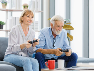 Obraz premium Caucasian old senior elderly lovely happy grandparents married couple husband and wife sitting playing competition on console video game together in living room