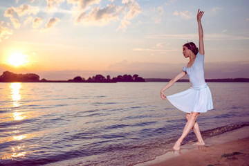 Fototapeta na wymiar Passion To Dance With Japanese Ballet Dancer in White Dress And Silver Crown Standing In Ocean Waves And Showing Ballet Pas With Lifted Hand Against Picturesque Sunset At Sea