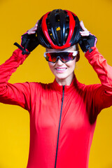 Cycling Ideas. Portrait of Positive Female Road Cyclist in Professional Outfit Posing Against Yellow Background While Putting On Helmet.