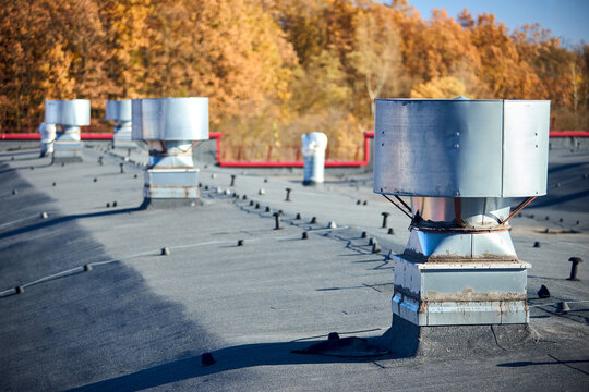Air roof exhaust ventilation fan system of industrial large commercial building with hooded chimneys flues and ducts in row on roof top selective focus with lightning protection system.