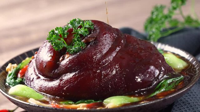 Pouring savory soy sauce with spoon over Taiwanese braised pork hock food in a plate.