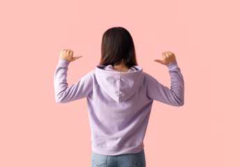 Beautiful young woman in stylish hoodie on color background, back view