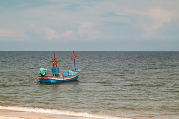 Naklejka na ściany i meble Fisherman boat float in the sea ocean near sand beach shore with hazy blue sky background landscape