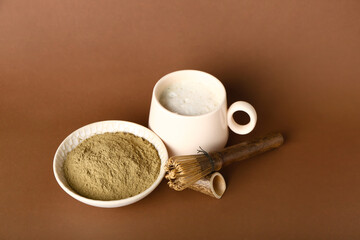 Bowl with hojicha powder, cup of tea and chasen on brown background