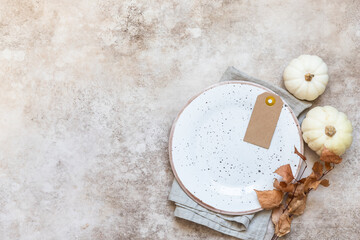 Festive autumn table place setting. Decorative white pumpkin, autumn leaves, craft ceramic plate and cutlery on concrete background. Fall composition. Flat lay, top view.