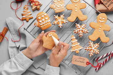 Woman decorating Christmas gingerbread cookies on light background