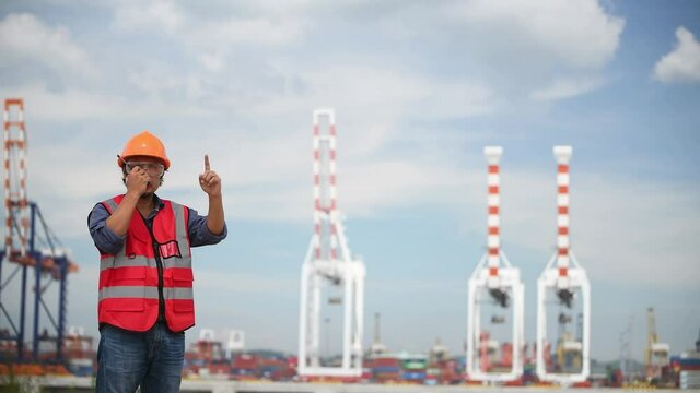 Engineer wearing safety uniform and helmet looking detail document on hand with logistic in habour backgroud.