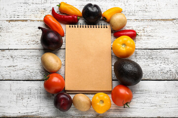 Blank notebook, fresh vegetables and fruits on light wooden background. Vegan Day