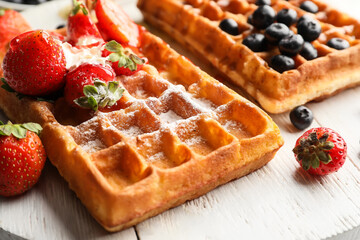 Tasty Belgian Waffles with berries on wooden board, closeup