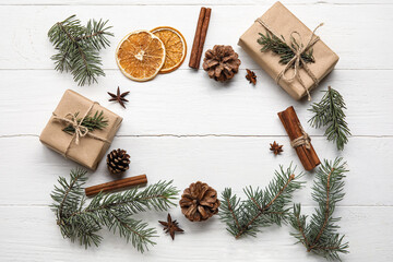 Frame made of fir tree branches, gift boxes, cinnamon, anise and slices of dried orange on white wooden background