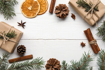 Frame made of fir tree branches, gift boxes, anise, cinnamon and slices of dried orange on white wooden background