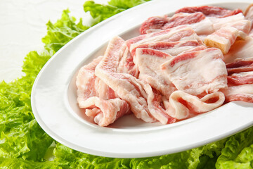 Plate with slices of uncooked bacon on white background, closeup