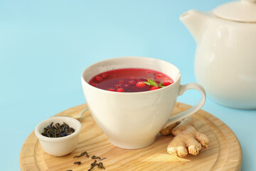 Wooden board with cup of tasty lingonberry tea on color background, closeup