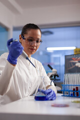 Physician researcher dropping liquid in medical glassware using micropipette analyzing coronavirus...